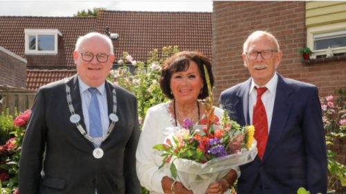 Burgemeester Frans Backhuijs met 2 bossen bloemen naar jubilarissen