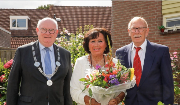 Burgemeester Frans Backhuijs met 2 bossen bloemen naar jubilarissen